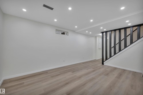 Spacious room featuring light wood-finish flooring, recessed lighting, a horizontal window, and a staircase with dark balusters and handrail - 3607 53 Street, Wetaskiwin, AB - Indoor