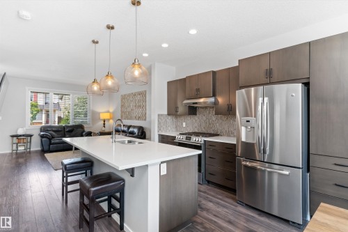 Modern kitchen featuring a large center island with integrated sink, stainless steel appliances, and wood-finish cabinetry - 3456 Cutler Crescent Sw, Edmonton, AB - Indoor Photo Showing Kitchen With Upgraded Kitchen