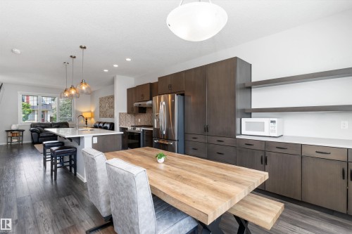 Open-concept kitchen and dining area featuring wood-finish flooring, dark wood cabinetry with matte black hardware, and an island with pendant lighting - 3456 Cutler Crescent Sw, Edmonton, AB - Indoor