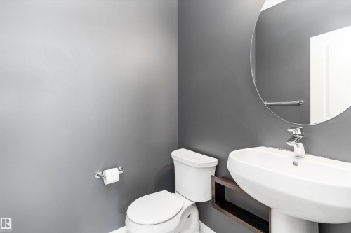 Powder room featuring a pedestal sink, round wall mirror, modern faucet, and dark wood-finish shelf - 3456 Cutler Crescent Sw, Edmonton, AB - Indoor Photo Showing Bathroom