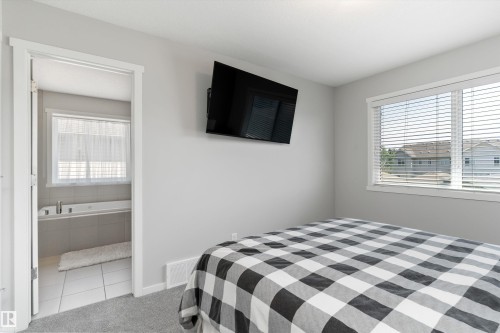 Carpeted bedroom with a window featuring horizontal blinds, direct access to a bathroom, and light gray walls - 3456 Cutler Crescent Sw, Edmonton, AB - Indoor Photo Showing Bedroom