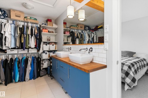 Walk-in closet featuring extensive wire shelving and hanging storage, dual vessel sinks on a wood-finish countertop, blue cabinetry, and white subway tile backsplash - 3456 Cutler Crescent Sw, Edmonton, AB - Indoor With Storage
