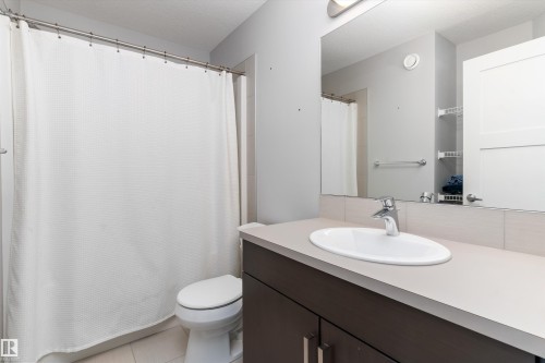 Contemporary bathroom featuring a dark wood-finish vanity with a light-toned countertop, an oval undermount sink, and a chrome faucet - 3456 Cutler Crescent Sw, Edmonton, AB - Indoor Photo Showing Bathroom