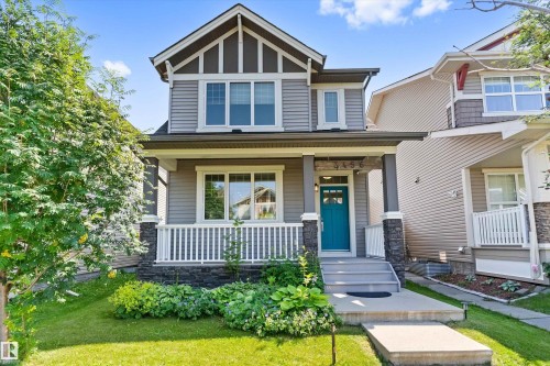 Two-story residence featuring a covered front porch with white railing, stone accents on columns and foundation, a vibrant turquoise entry door with glass inserts, and a concrete pathway - 3456 Cutler Crescent Sw, Edmonton, AB - Outdoor With Deck Patio Veranda With Facade