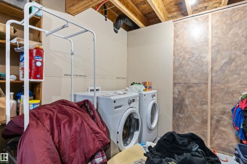 Dedicated laundry area featuring a front-load washer and dryer, exposed ceiling joists, partially finished walls, and built-in shelving - 3456 Cutler Crescent Sw, Edmonton, AB - Indoor Photo Showing Laundry Room