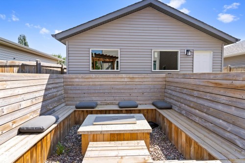 Hardscaped patio area featuring built-in wooden bench seating, a central fire pit with a stone surround, and gravel landscaping - 3456 Cutler Crescent Sw, Edmonton, AB - Outdoor With Exterior