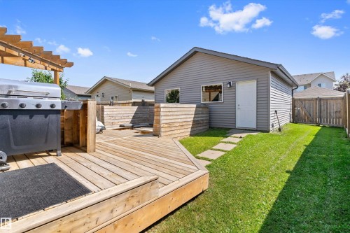 Spacious backyard featuring a multi-level wood deck with a pergola, a detached garage with vinyl siding and a side entry door, a manicured lawn, and a privacy fence - 3456 Cutler Crescent Sw, Edmonton, AB - Outdoor With Exterior