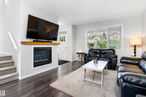 Living area featuring wood-finish flooring, a contemporary fireplace with a wooden mantel, and white trim - 3456 Cutler Crescent Sw, Edmonton, AB - Indoor Photo Showing Living Room With Fireplace