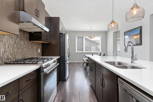 Modern kitchen featuring dark wood-finish cabinetry, stainless steel appliances, white countertops, and a full-height mosaic tile backsplash - 3456 Cutler Crescent Sw, Edmonton, AB - Indoor Photo Showing Kitchen With Double Sink With Upgraded Kitchen