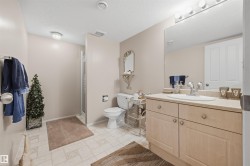 Bathroom featuring a light-toned vanity with an integrated sink, a large wall-mounted mirror with overhead bar lighting, a white toilet, and a glass-enclosed shower - 