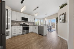 Open-concept kitchen featuring white cabinetry, stainless steel appliances, wood-finish flooring, a tiled backsplash, and recessed lighting - 