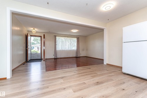 Open concept living space featuring light wood-finish flooring, a broad entryway, and a prominent front door with screen door - 4812 105B Street Nw, Edmonton, AB - Indoor Photo Showing Other Room