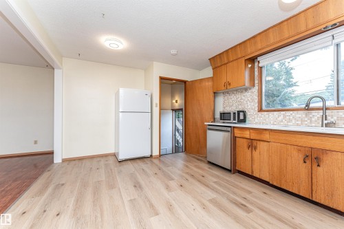 Kitchen featuring wood-finish flooring, wood cabinetry, stainless steel dishwasher, and a tile backsplash - 4812 105B Street Nw, Edmonton, AB - Indoor Photo Showing Kitchen