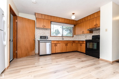 Kitchen featuring wood cabinetry, a mosaic tile backsplash, and wood-finish flooring - 4812 105B Street Nw, Edmonton, AB - Indoor Photo Showing Kitchen