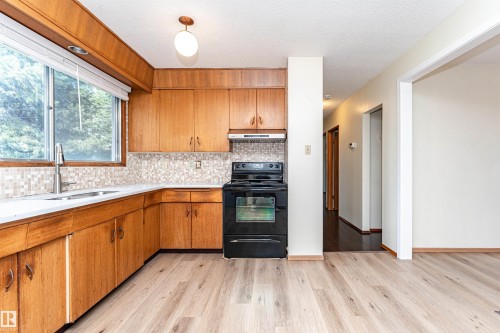 Kitchen featuring wood cabinetry, white countertops, tile backsplash, and a black oven range - 4812 105B Street Nw, Edmonton, AB - Indoor Photo Showing Kitchen