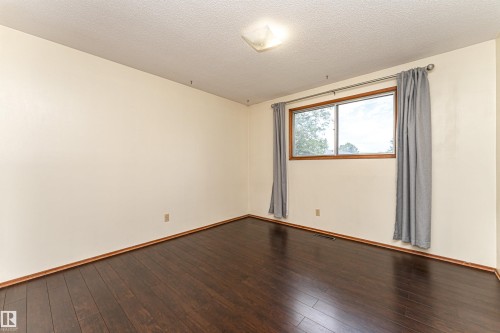Spacious room featuring dark wood-finish flooring, a neutral wall color, and a window with wood trim - 4812 105B Street Nw, Edmonton, AB - Indoor Photo Showing Other Room