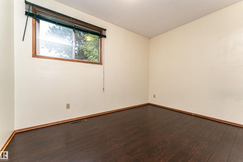 Room featuring wood-finish flooring, light-toned walls, a window with wood trim, and horizontal blinds - 4812 105B Street Nw, Edmonton, AB - Indoor Photo Showing Other Room