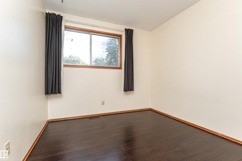 Bright room featuring a large window with natural wood trim, dark wood-finish flooring, and light-colored walls - 4812 105B Street Nw, Edmonton, AB - Indoor Photo Showing Other Room