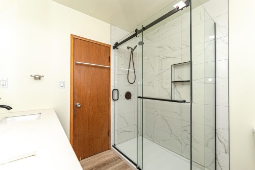 Contemporary shower enclosure featuring clear glass panels, a sliding barn door style frame, and a built-in niche with shelving - 4812 105B Street Nw, Edmonton, AB - Indoor Photo Showing Bathroom