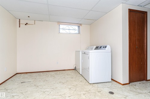 Utility area featuring a window, tile-finish flooring, a suspended ceiling, and a wooden bi-fold door - 4812 105B Street Nw, Edmonton, AB - Indoor Photo Showing Laundry Room