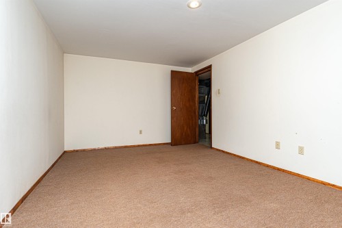 Neutral-toned carpeted room featuring white walls, wood baseboards, a recessed ceiling light, and a brown interior door - 4812 105B Street Nw, Edmonton, AB - Indoor Photo Showing Other Room