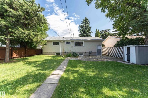 Expansive backyard featuring a concrete pathway, a detached storage shed, and mature trees providing natural shade - 4812 105B Street Nw, Edmonton, AB - Outdoor