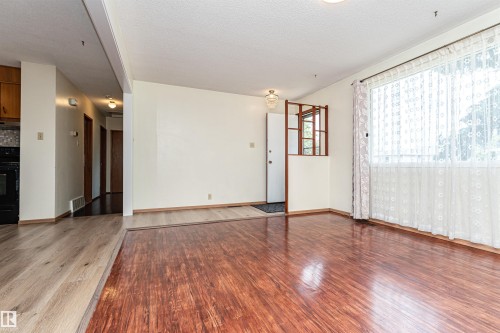 Living area featuring wood-finish flooring, a large window with sheer curtains, and a decorative interior half-wall with wood accents - 4812 105B Street Nw, Edmonton, AB - Indoor Photo Showing Other Room