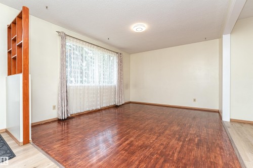 Spacious room featuring wood-finish flooring, a large window, a built-in wood-toned shelving unit, and a flush-mount ceiling light fixture - 4812 105B Street Nw, Edmonton, AB - Indoor Photo Showing Other Room