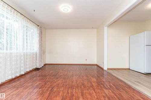 Spacious interior featuring wood-finish flooring, a broad window with sheer and patterned curtains, and crown molding - 4812 105B Street Nw, Edmonton, AB - Indoor Photo Showing Other Room