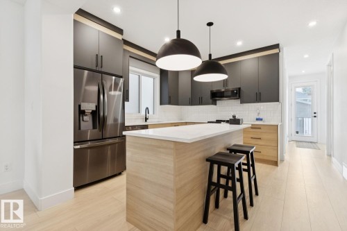 Modern kitchen featuring light wood-finish flooring, dark cabinetry, stainless steel appliances, a center island with a light countertop, and dual pendant lighting - 10531 67 Avenue Nw, Edmonton, AB - Indoor Photo Showing Kitchen With Upgraded Kitchen