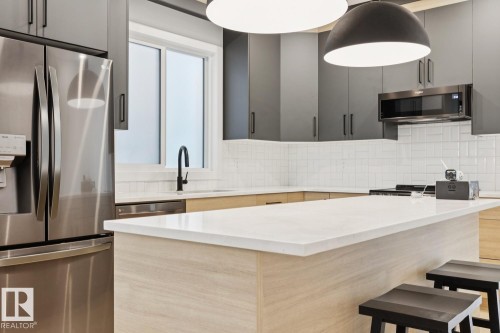 Modern kitchen featuring a white subway tile backsplash, light wood-finish lower cabinetry, and dark gray upper cabinetry - 10531 67 Avenue Nw, Edmonton, AB - Indoor Photo Showing Kitchen With Upgraded Kitchen