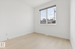 Bright interior space featuring light wood-finish flooring, white walls, and a large window with a roller shade - 
