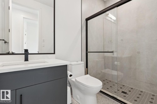 Modern bathroom featuring a dark gray vanity with a white countertop, an undermount sink, and a matte black faucet - 10531 67 Avenue Nw, Edmonton, AB - Indoor Photo Showing Bathroom