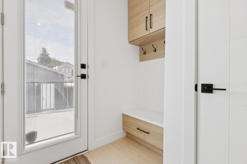 Entryway featuring a full-light door with integrated blinds, wood-finish built-in storage with upper cabinetry, a bench with a drawer, and coat hooks, complemented by wood-finish flooring - 10531 67 Avenue Nw, Edmonton, AB - Indoor Photo Showing Other Room
