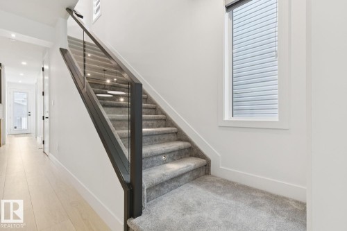 Staircase featuring a glass railing with dark wood-finish newel posts and handrail, carpeted treads with recessed lighting, and a prominent window - 10531 67 Avenue Nw, Edmonton, AB - Indoor Photo Showing Other Room