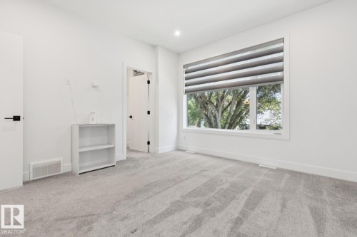 Bright interior room featuring a large window with horizontal blinds, light gray carpeting, and white walls - 10531 67 Avenue Nw, Edmonton, AB - Indoor Photo Showing Other Room