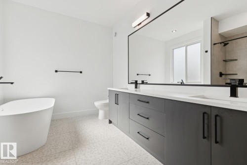 Contemporary bathroom featuring a dual vanity with dark gray cabinetry and matte black hardware, a large frameless mirror, a freestanding soaking tub, and a shower with built-in shelving - 10531 67 Avenue Nw, Edmonton, AB - Indoor Photo Showing Bathroom