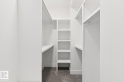 Walk-in closet featuring white built-in shelving, hanging rods, and gray carpeting - 