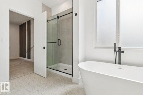 Freestanding soaking tub with a matte black floor-mounted faucet, glass-enclosed shower with sliding door, large format wall tiling, and textured tile flooring - 10531 67 Avenue Nw, Edmonton, AB - Indoor Photo Showing Bathroom