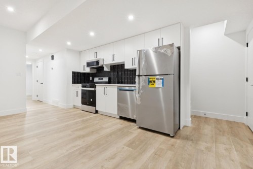 Contemporary kitchen featuring white cabinetry, stainless steel appliances, a black subway tile backsplash, and light wood-finish flooring - 10531 67 Avenue Nw, Edmonton, AB - Indoor Photo Showing Kitchen