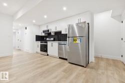 Contemporary kitchen featuring white cabinetry, stainless steel appliances, a black subway tile backsplash, and light wood-finish flooring - 