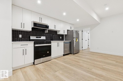 Kitchenette featuring white cabinetry, dark subway tile backsplash, stainless steel appliances, and wood-finish flooring - 10531 67 Avenue Nw, Edmonton, AB - Indoor Photo Showing Kitchen