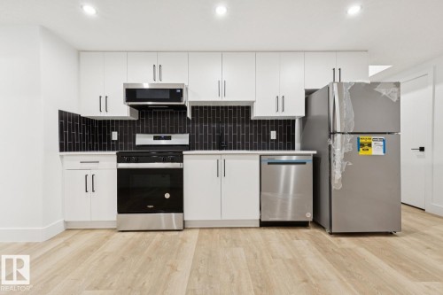 Contemporary kitchen featuring white cabinetry, stainless steel appliances, a black subway tile backsplash, light wood-finish flooring, and recessed lighting - 10531 67 Avenue Nw, Edmonton, AB - Indoor Photo Showing Kitchen