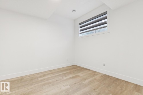 Bright interior space featuring light wood-finish flooring, white baseboards, and a window with horizontal blinds - 10531 67 Avenue Nw, Edmonton, AB - Indoor Photo Showing Other Room