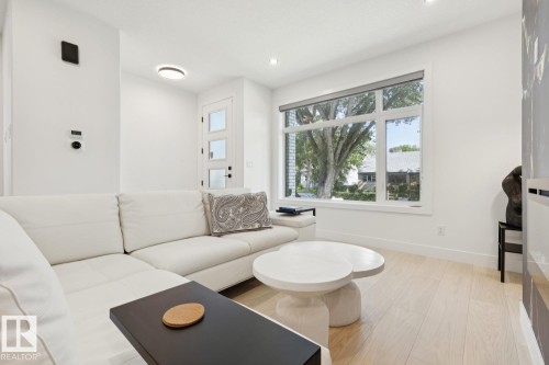 Bright living space featuring light wood-finish flooring, a large window, a modern entry door with frosted glass panels, recessed lighting, and white walls throughout - 10531 67 Avenue Nw, Edmonton, AB - Indoor Photo Showing Living Room