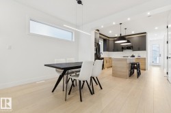 Open-concept kitchen and dining area featuring light wood-finish flooring, a kitchen island with seating, dark shaker-style upper cabinetry, and a white subway tile backsplash - 