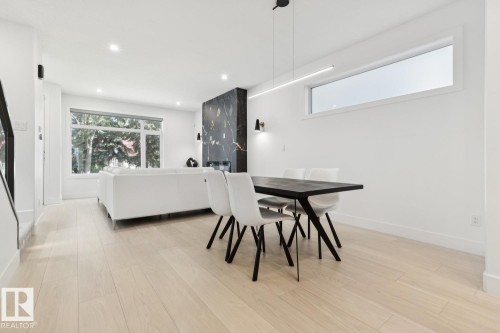 Open-concept living area featuring light wood-finish flooring, recessed lighting, and a prominent dark marble-look fireplace surround - 10531 67 Avenue Nw, Edmonton, AB - Indoor