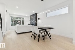 Open-concept living area featuring light wood-finish flooring, recessed lighting, and a prominent dark marble-look fireplace surround - 