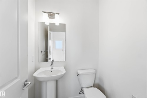 Pedestal sink with chrome faucet, rectangular mirror, and a two-bulb wall sconce - 223 157 Avenue Ne, Edmonton, AB - Indoor Photo Showing Bathroom