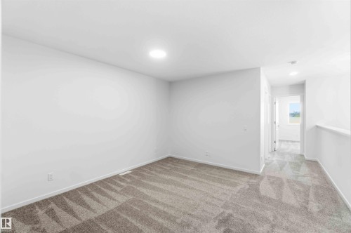 Carpeted room featuring recessed lighting and neutral wall tones, with an adjacent hallway and window offering natural illumination - 223 157 Avenue Ne, Edmonton, AB - Indoor Photo Showing Other Room